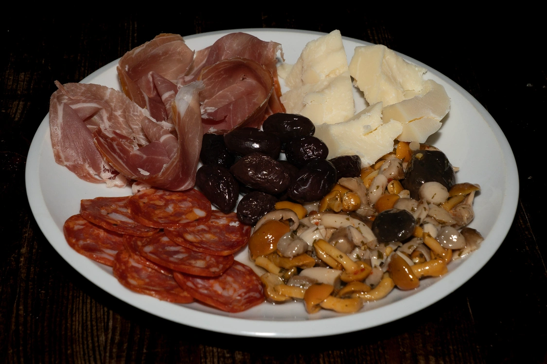Piatto di antipasto misto con prosciutto crudo, scaglie di grana, olive nere, salame piccante e una selezione di funghi e verdure sott'olio — Pizzeria Alla Botte, Misilmeri.