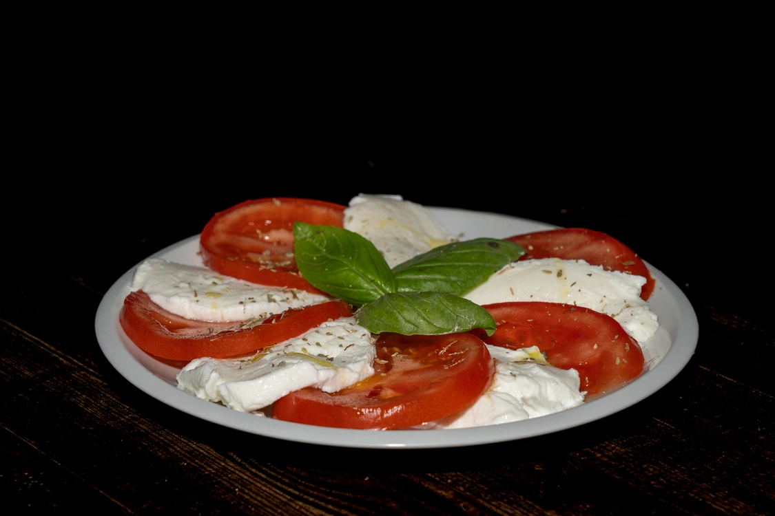 Antipasto Caprese con fette alternate di pomodoro rosso fresco e mozzarella bianca, guarnite con foglie di basilico verde al centro e una spolverata di origano — Pizzeria Alla Botte, Misilmeri.