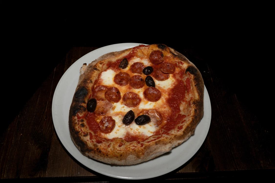 Pizza alla Diavola con base rossa di pomodoro, fior di latte filante, fette di salame piccante e olive nere intere — Pizzeria Alla Botte, Misilmeri.
