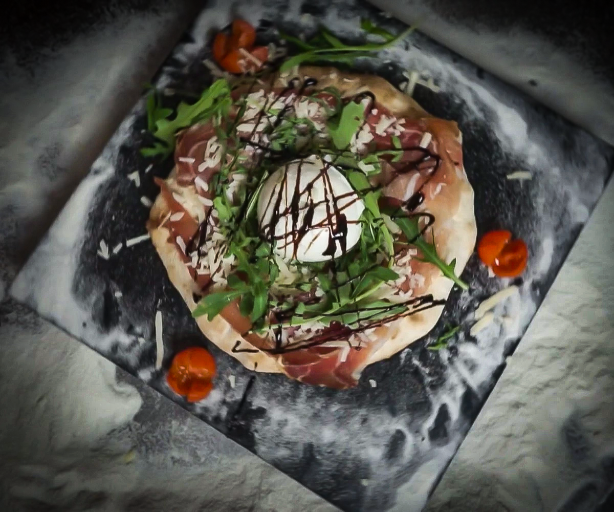 Pizza Corona con impasto integrale, cornicione ripieno, bocconcino di bufala centrale, crudo, rucola, scaglie di grana e glassa balsamica della Pizzeria "Alla Botte" a Misilmeri.