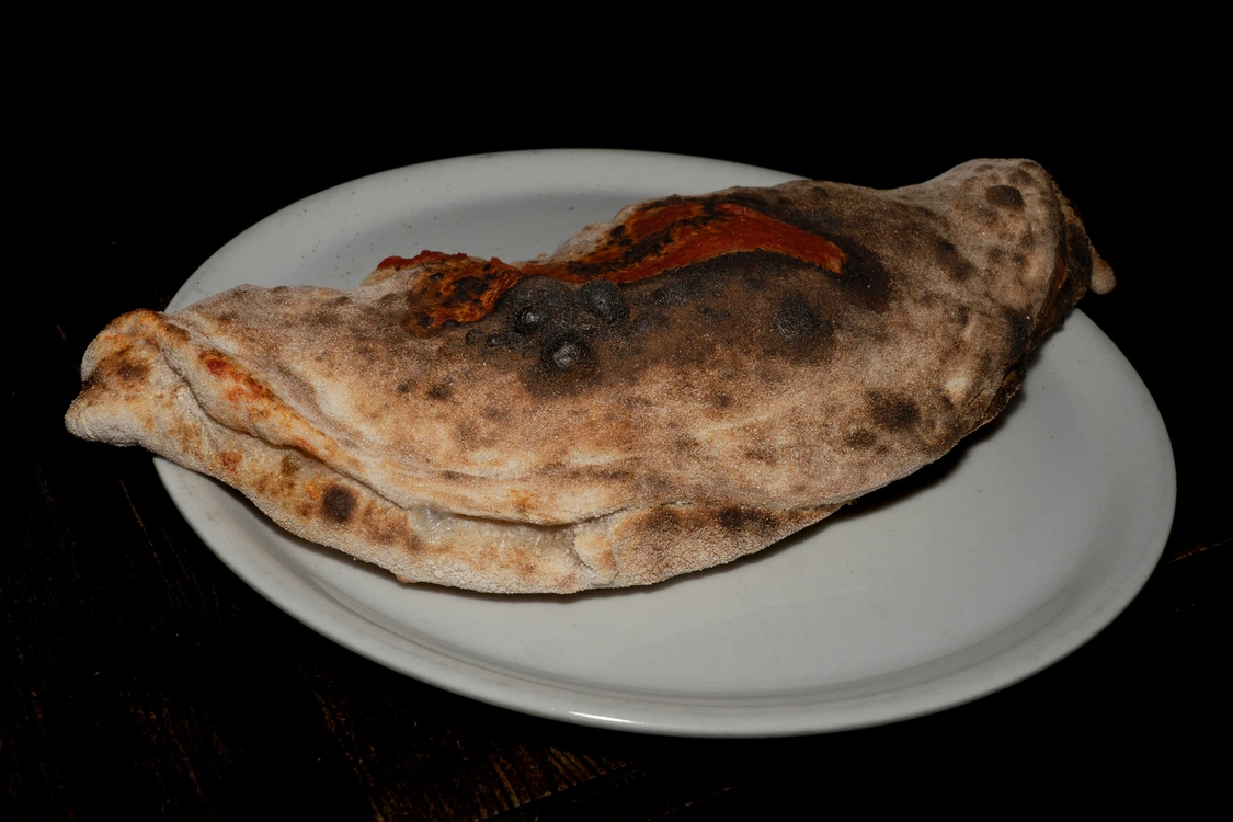 Pizza Calzone dorato cotto nel forno a legna, farcito con pomodoro, fior di latte e prosciutto — Pizzeria Alla Botte, Misilmeri.