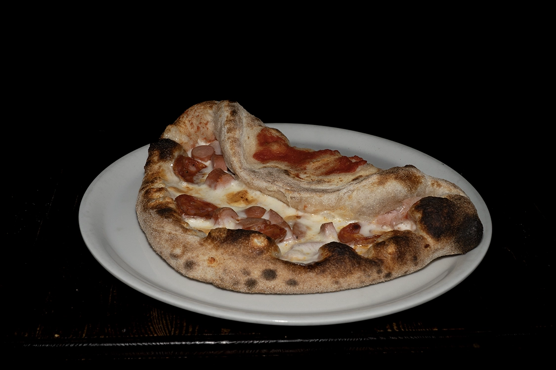 Calzonpizza a Misilmeri con cuore di prosciutto e fior di latte, guarnito esternamente con wurstel e salame piccante — Pizzeria Alla Botte.