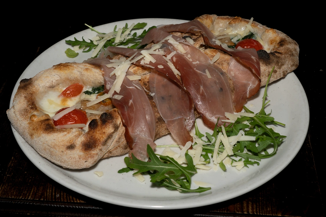 Pizza Cannolo dalla forma allungata farcita con mozzarella di bufala, pomodorini, spinaci e funghi porcini, sormontata da fette di speck crudo e scaglie di grana su un letto di rucola — Pizzeria Alla Botte, Misilmeri.