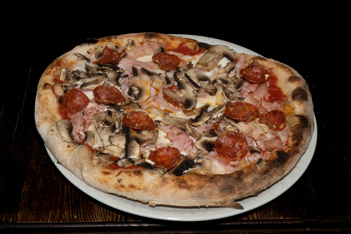 Pizza Love Story con base pomodoro e fior di latte, farcita con prosciutto cotto, funghi freschi affettati e rondelle di salame piccante, cotta nel forno a legna — Pizzeria Alla Botte, Misilmeri.