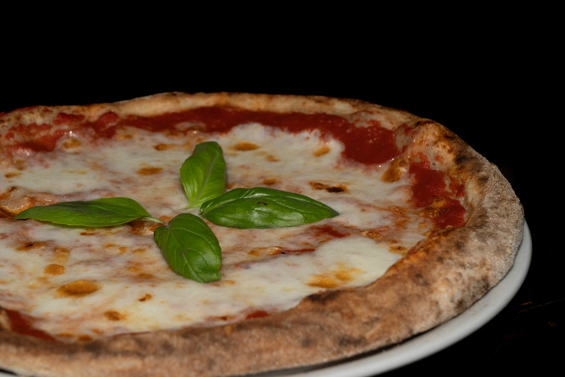 Pizza Margherita artigianale con base di pomodoro rosso saporito, fior di latte fuso e foglie di basilico fresco al centro, cotta in forno a legna — Pizzeria Alla Botte, Misilmeri.