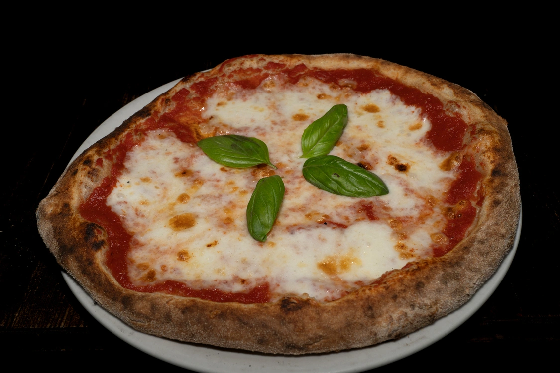 Pizza Mediterranea con base di pomodoro, fior di latte fuso, olio all'aglio e foglie di basilico fresco disposte a raggiera, cotta in forno a legna — Pizzeria Alla Botte, Misilmeri.
