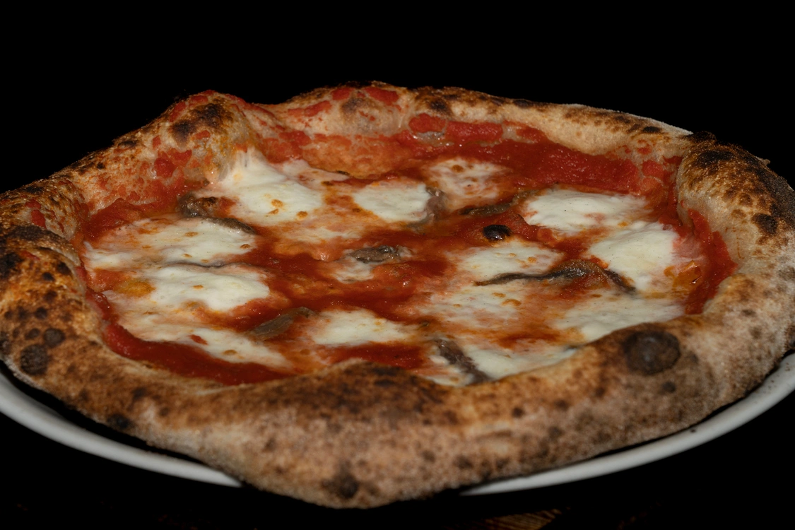 Pizza Napoli artigianale con base di pomodoro, fior di latte filante e filetti di acciughe saporite, caratterizzata da un cornicione alto e dorato — Pizzeria Alla Botte, Misilmeri.