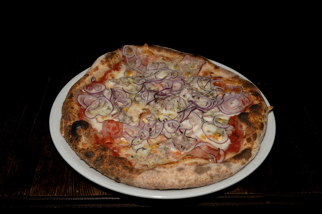 Pizza Pino con base pomodoro e fior di latte, arricchita da gorgonzola fuso, bocconcini di salsiccia, fette di bacon croccante e sottili anelli di cipolla rossa — Pizzeria Alla Botte, Misilmeri.