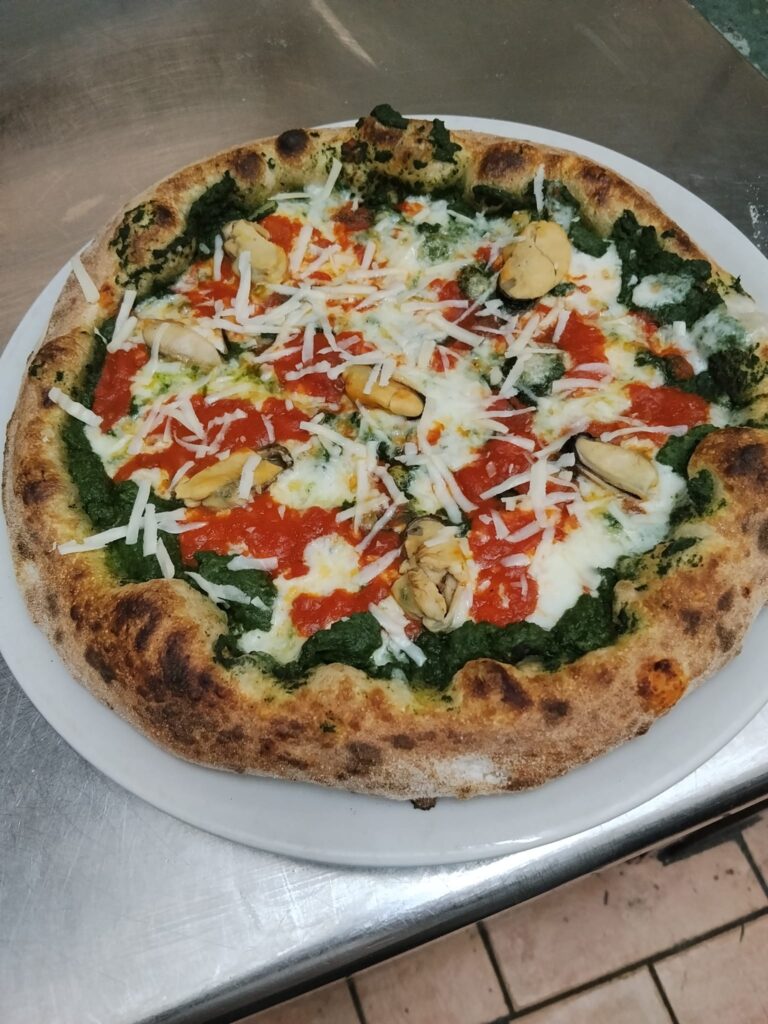 izza artigianale "Tenerumi e cozze" cotta nel forno a legna della Pizzeria Alla Botte a Misilmeri, condita con crema di tenerumi, mozzarella, salsa di pomodoro picchi pacchi, cozze e scaglie di pecorino siciliano.