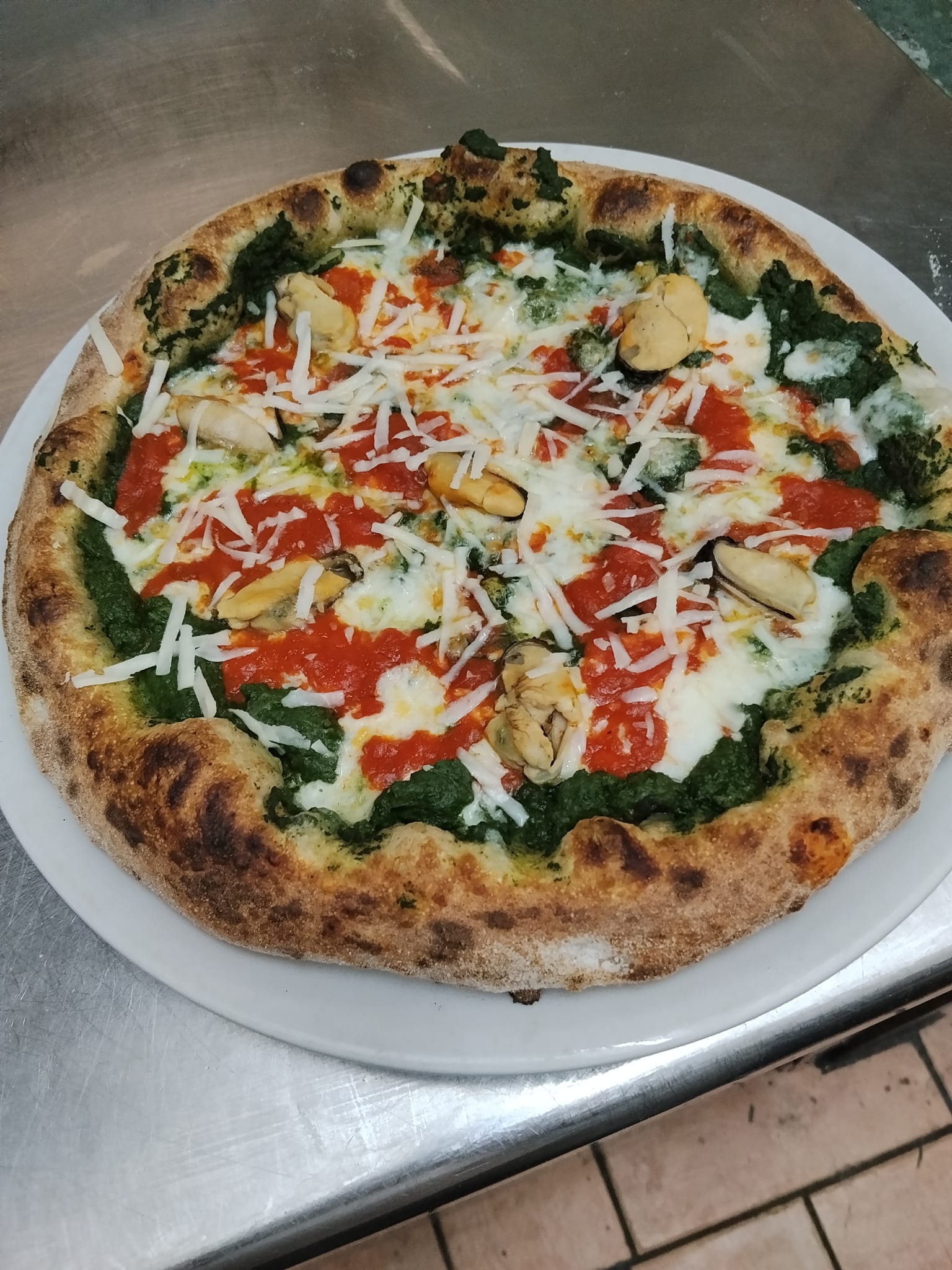 izza artigianale "Tenerumi e cozze" cotta nel forno a legna della Pizzeria Alla Botte a Misilmeri, condita con crema di tenerumi, mozzarella, salsa di pomodoro picchi pacchi, cozze e scaglie di pecorino siciliano.